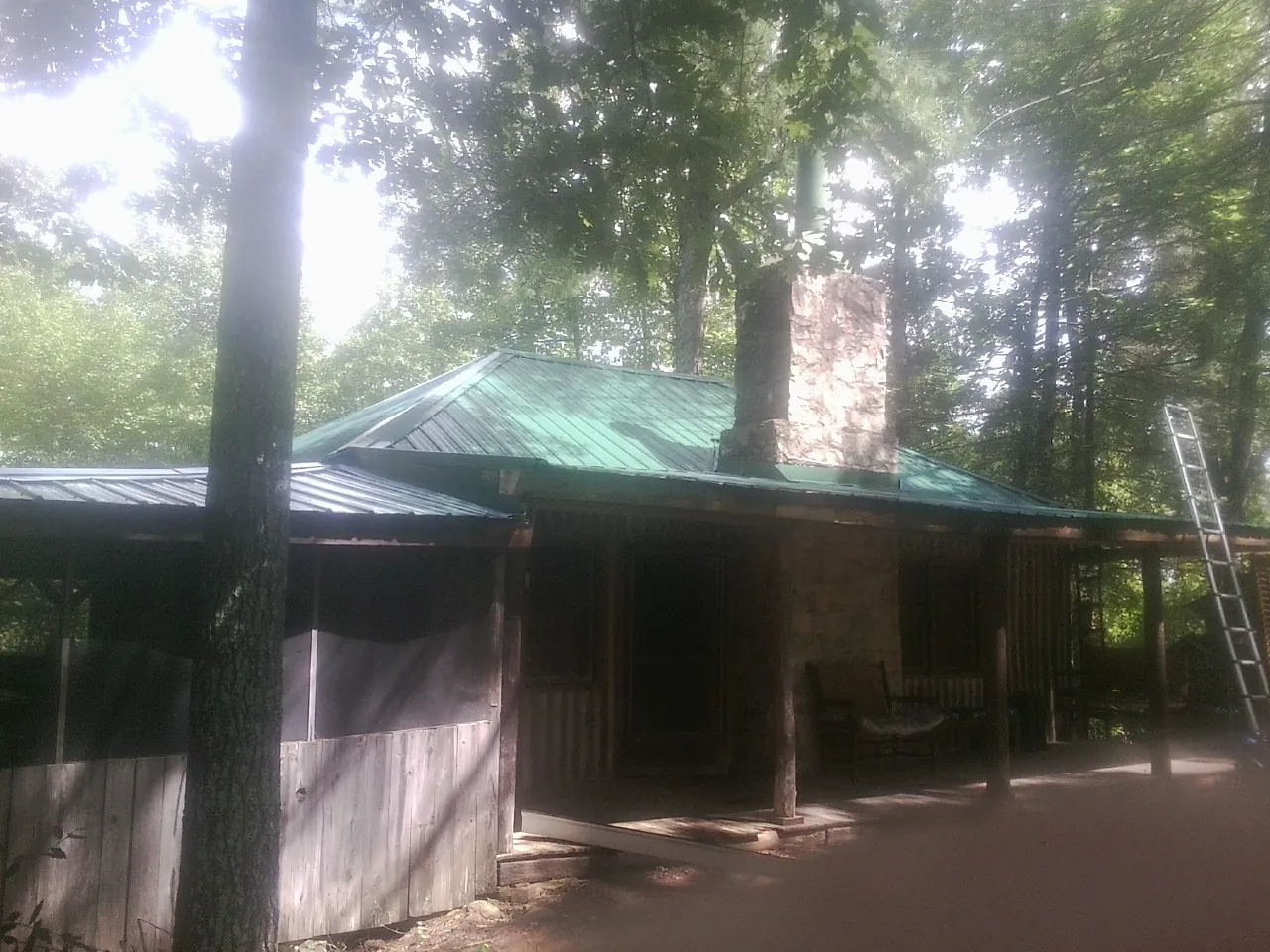 Green metal roof and stone chimney above a log cabin porch in Victoria